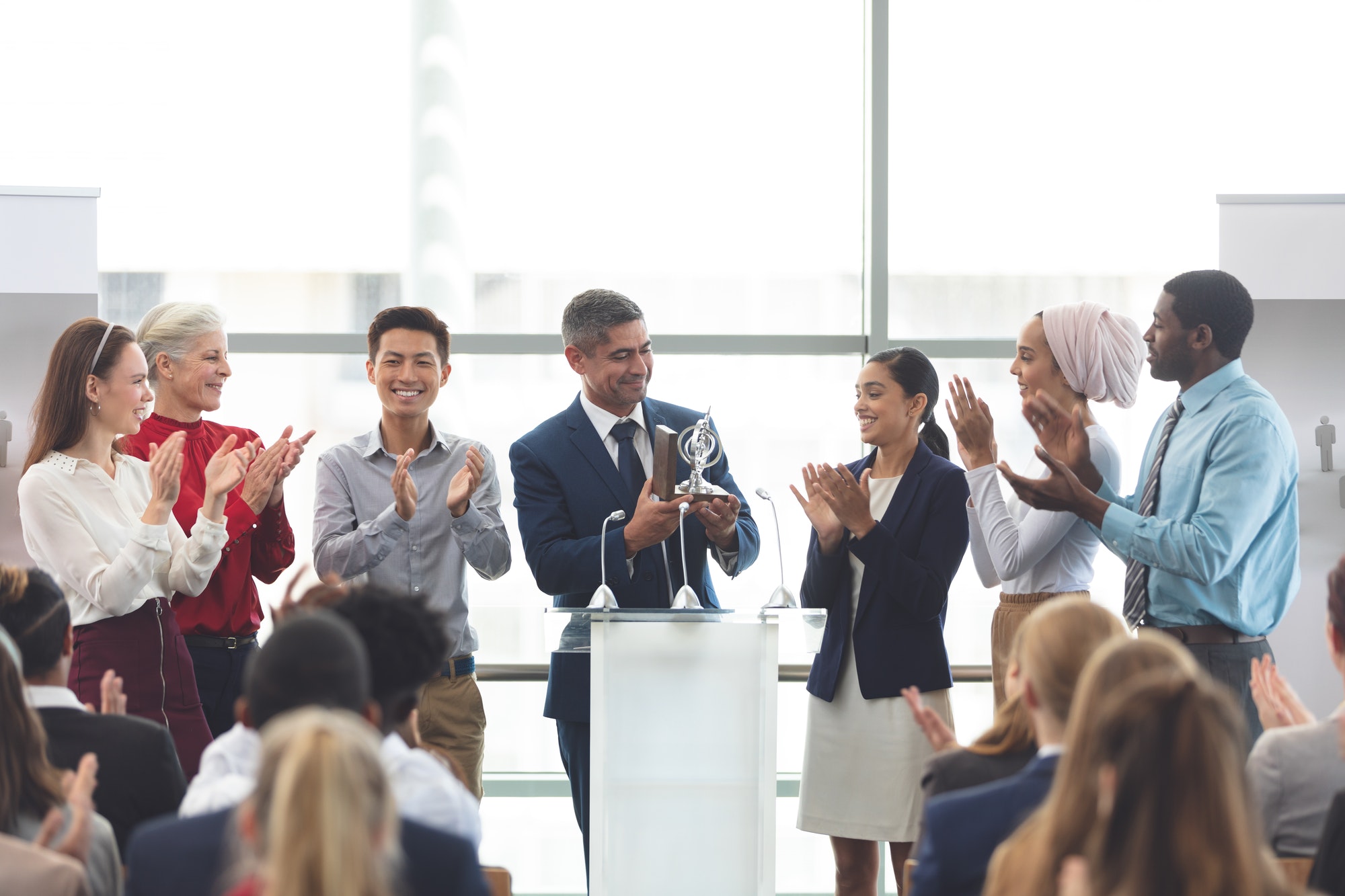 businessman-holding-award-on-podium-with-colleagues-at-business-seminar.jpg
